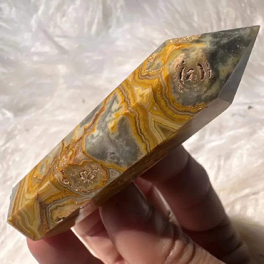 Crazy Lace Agate crystal tower with swirling bands of cream, rust, gold, and pink, held against a white background.