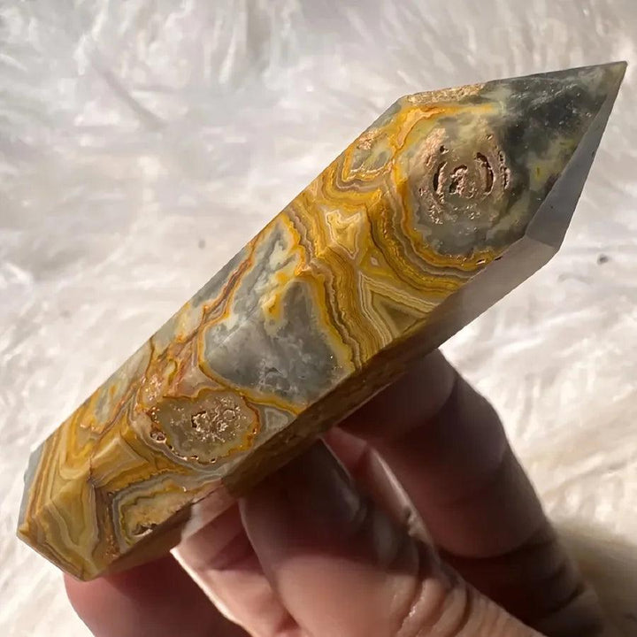 Crazy Lace Agate crystal tower with swirling bands of cream, rust, gold, and pink, held against a white background.