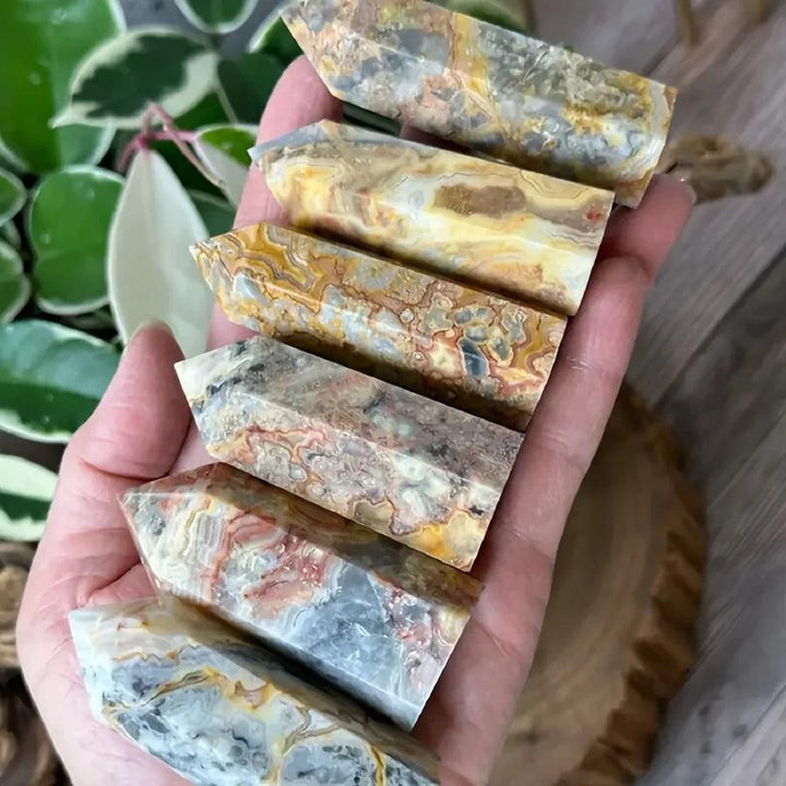 Hand holding six Crazy Lace Agate crystal towers with swirling bands of cream, rust, gold, and pink.