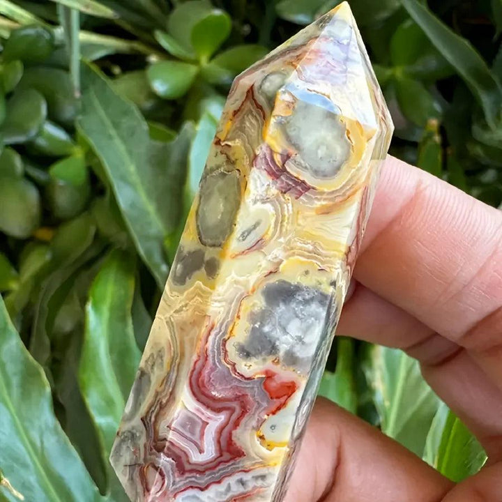 Hand holding a polished Crazy Lace Agate crystal tower with swirling bands of cream, rust, gold, and pink.