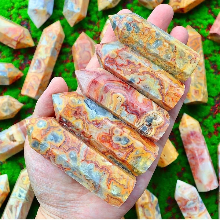 Hand holding multiple Crazy Lace Agate crystal towers with swirling bands of cream, rust, gold, and pink.