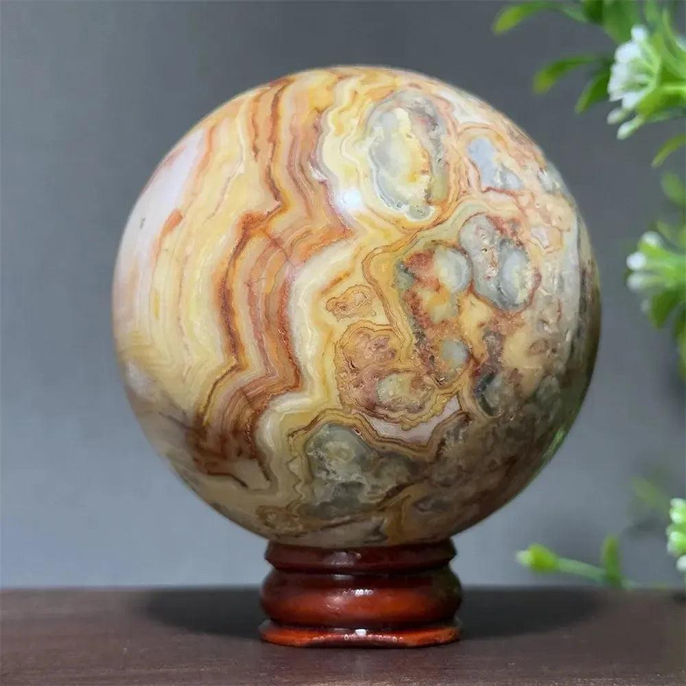 Polished Crazy Lace Agate sphere from Crystal Destiny, with swirling patterns of cream, brown, red, and gold on a wooden stand.