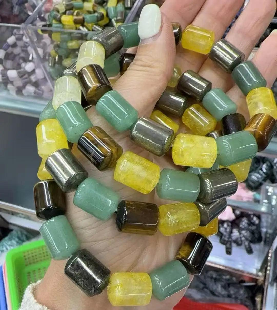 Hand holding a Crystal Big Beads Bracelet with barrel-cut beads in green, yellow, and tiger eye natural stones.