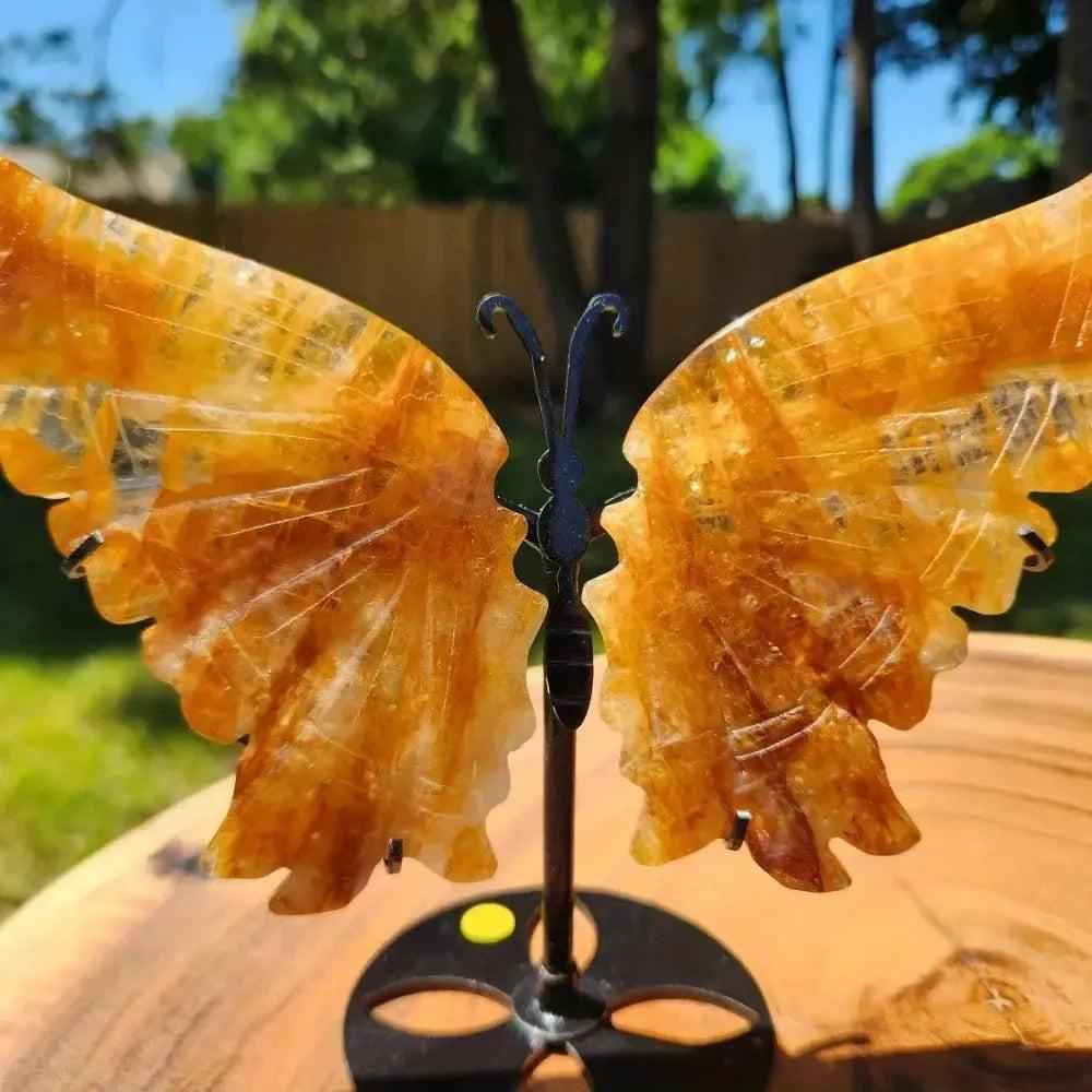 Golden Healer Quartz butterfly wings carving on a stand from Crystal Destiny, radiating warm energy.