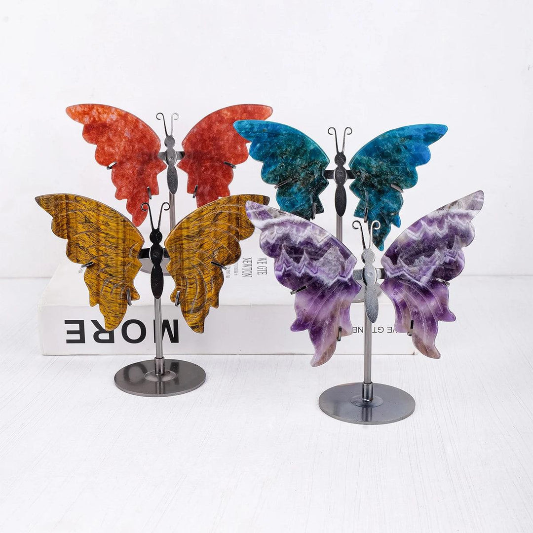 Polished crystal butterfly wings in various stones: red, blue, yellow Tiger Eye, and purple Amethyst, on metal stands.