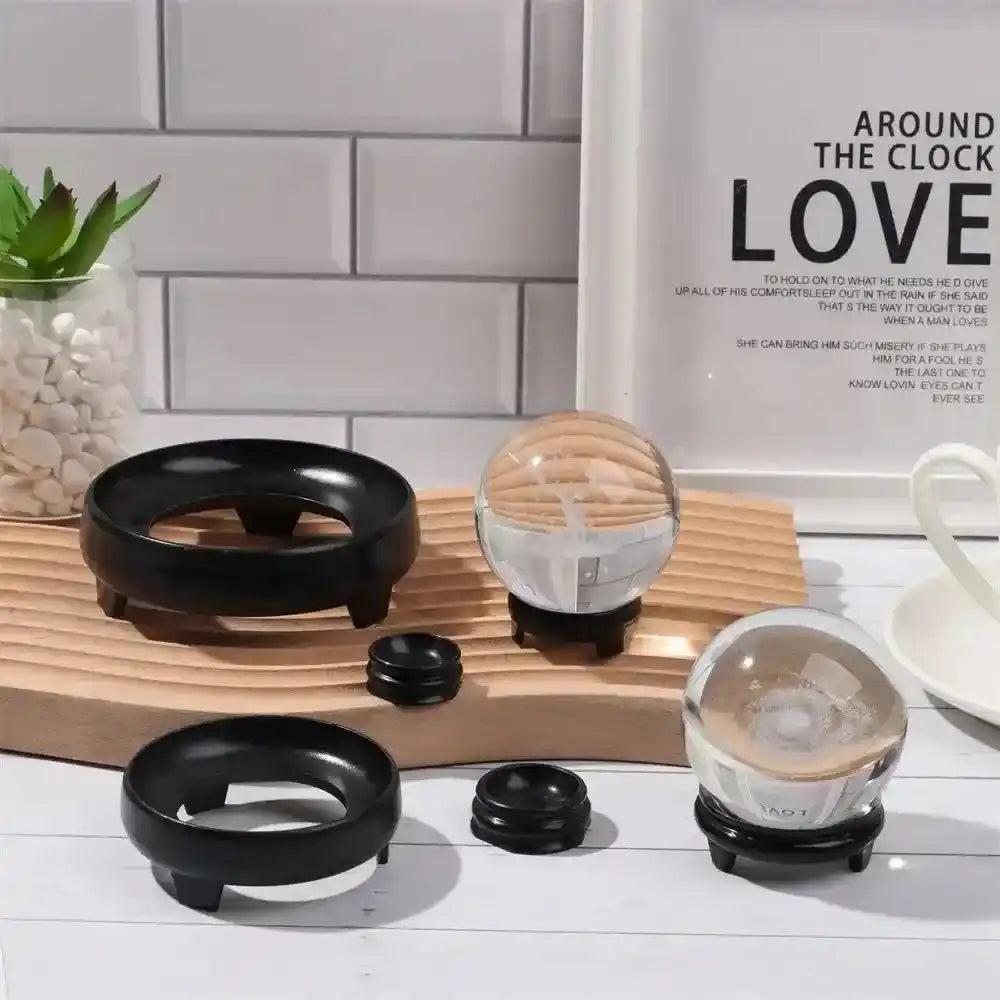 Assorted black crystal sphere display stands in various sizes, elegantly showcasing clear crystal spheres on a wooden surface.