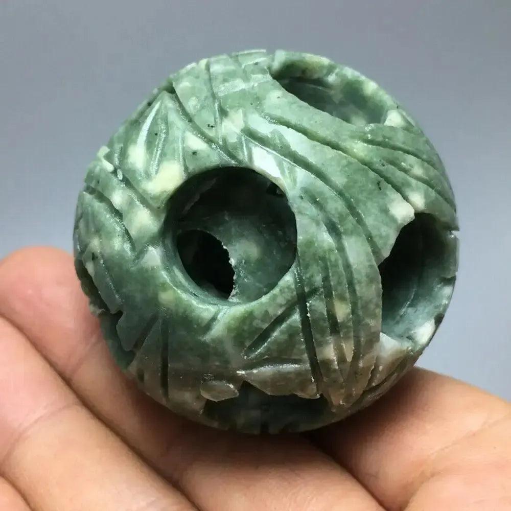 Hand-held cyan jade nested sphere carving with intricate openwork, symbolizing harmony and abundance.