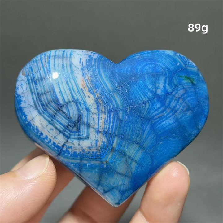 Vivid blue Dragon Veined Pattern Agate crystal heart, 89g, with swirling white and orange patterns, held in hand.
