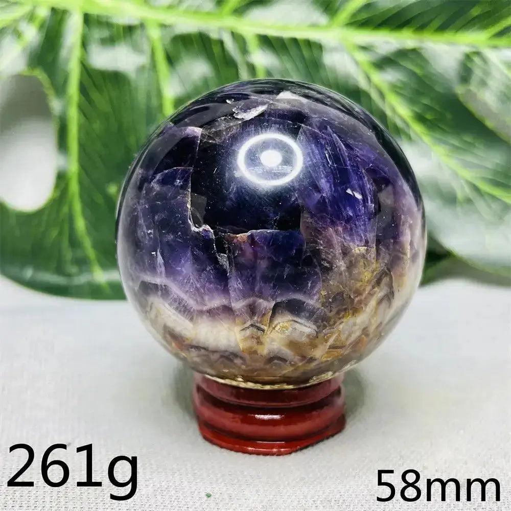 Crystal Destiny Dream Amethyst Geode Sphere, deep violet with sparkling clusters, on a red wooden stand.