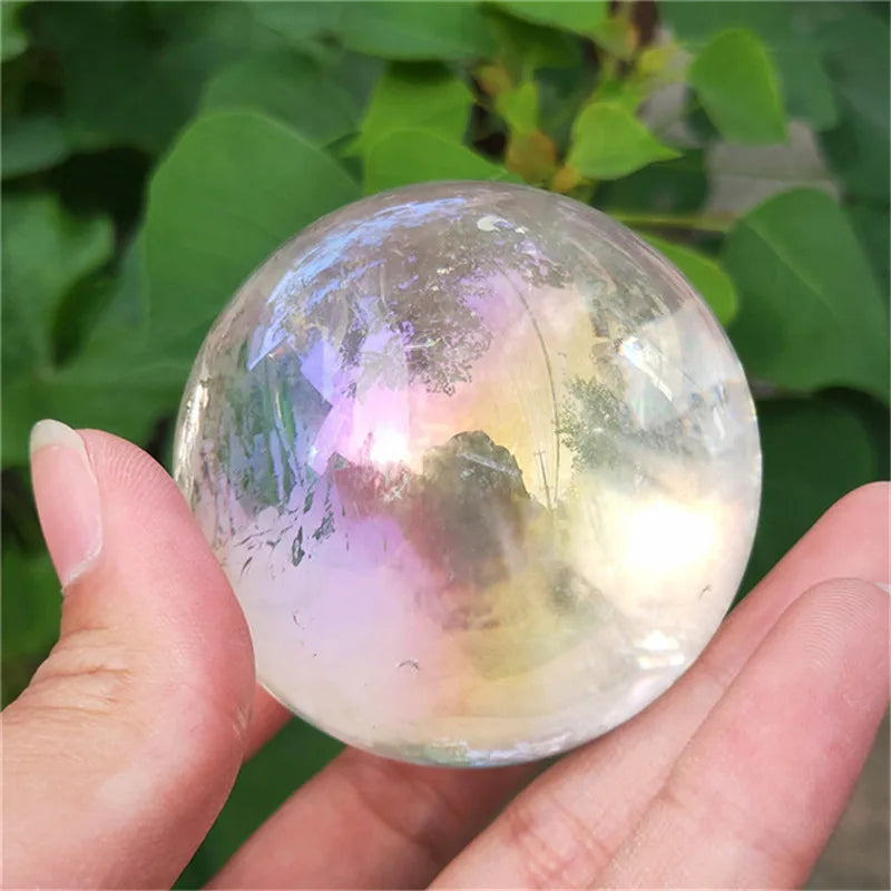 Electroplated Aura Clear Quartz sphere with iridescent rainbow shimmer held in hand for meditation and energy healing.