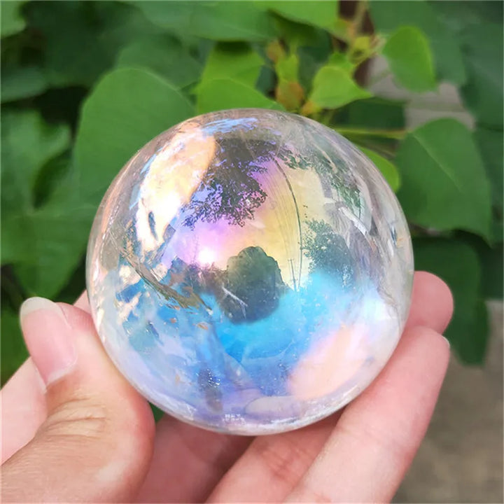 Electroplated Aura Clear Quartz sphere with a rainbow shimmer, held in hand to showcase its high-frequency energy.