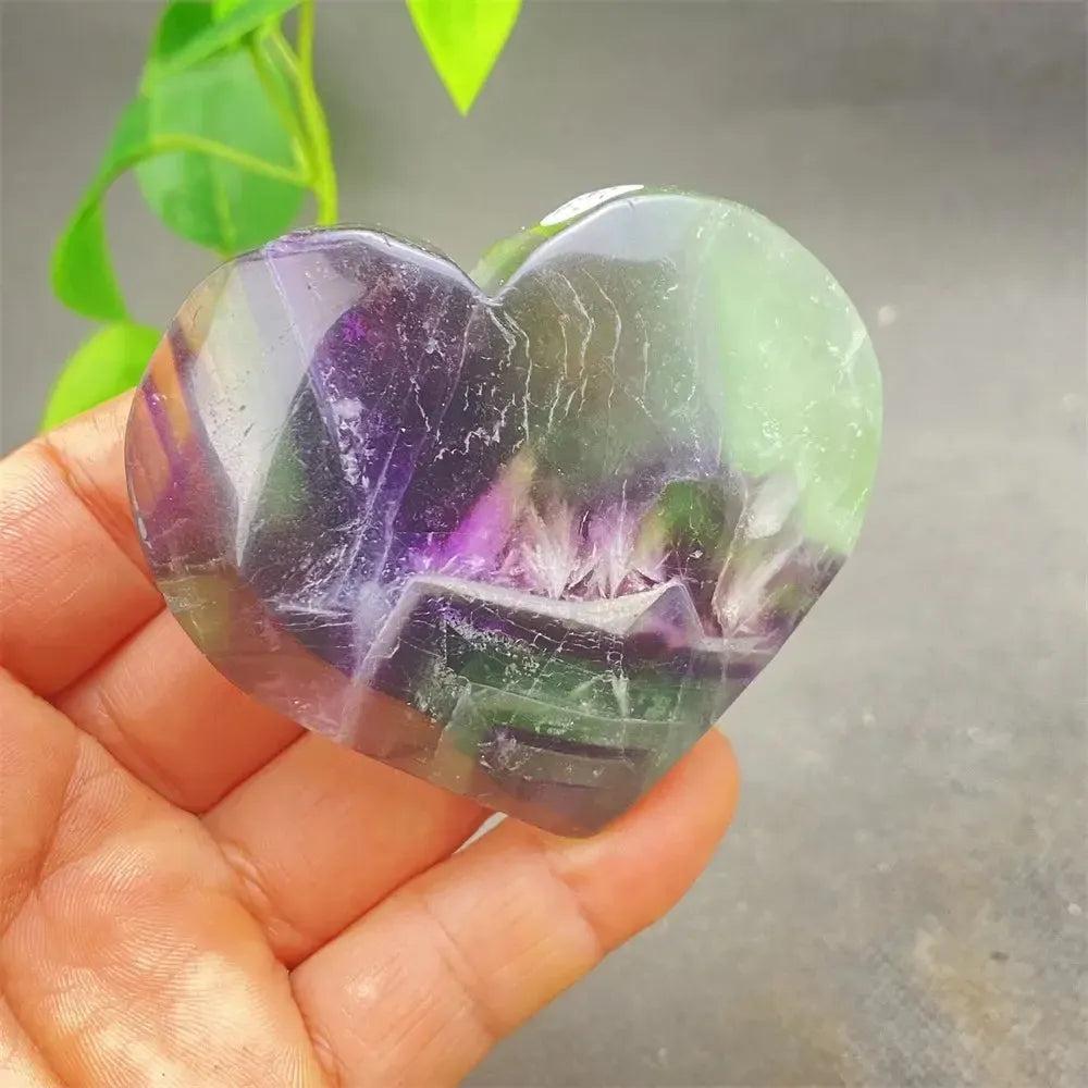 Polished Feather Fluorite Crystal Heart with vibrant purple, green, and clear bands, held in a hand.