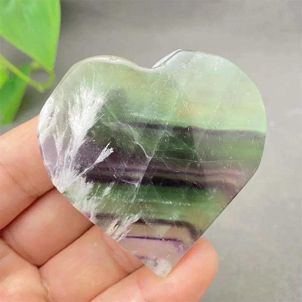 Polished Feather Fluorite Crystal Heart with stunning bands of purple, green, and clear tones, held in a hand.