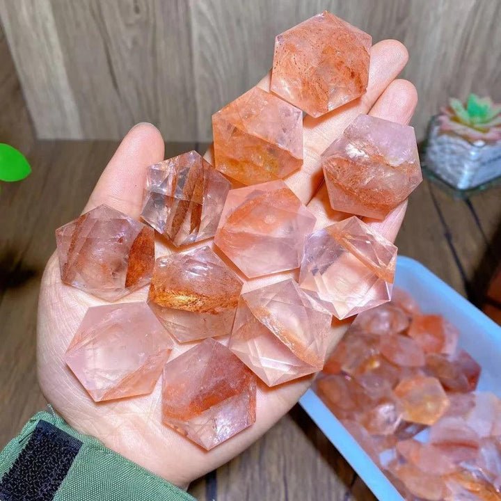 Hand holding multiple polished Fire Quartz hexagram star pendants, showcasing their dynamic red and clear hues.