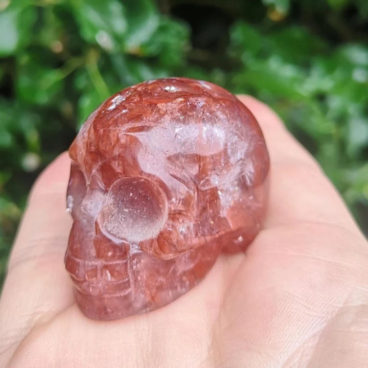 Handheld Natural Fire Quartz skull ornament featuring deep red inclusions, perfect for healing and unique holiday decor.