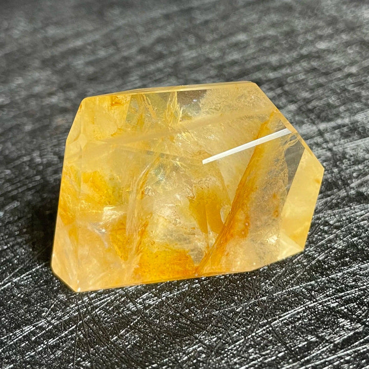 Polished Fire Quartz crystal freeform, glowing with warm amber and rust iron oxide inclusions, on a dark textured surface.