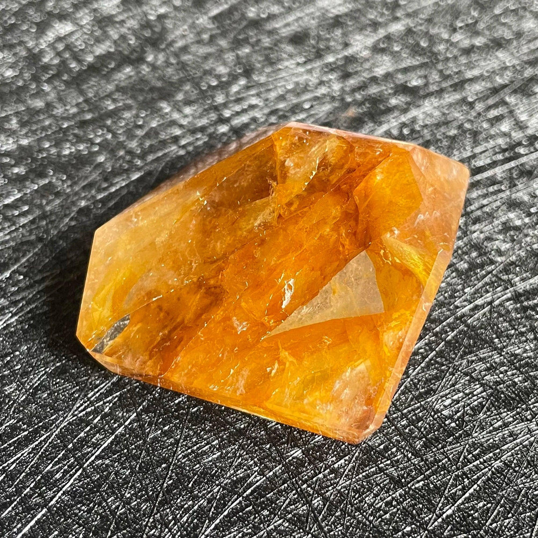 Polished Fire Quartz crystal freeform with warm orange and amber iron oxide inclusions, glowing on a dark textured surface.