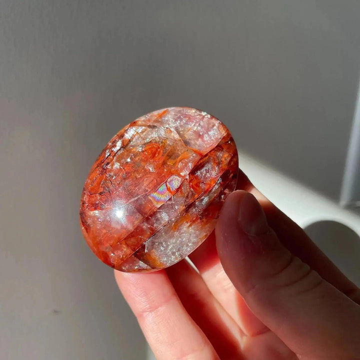 High-grade Fire Quartz palm stone, a smooth, polished crystal with fiery red hematite inclusions, held in hand.