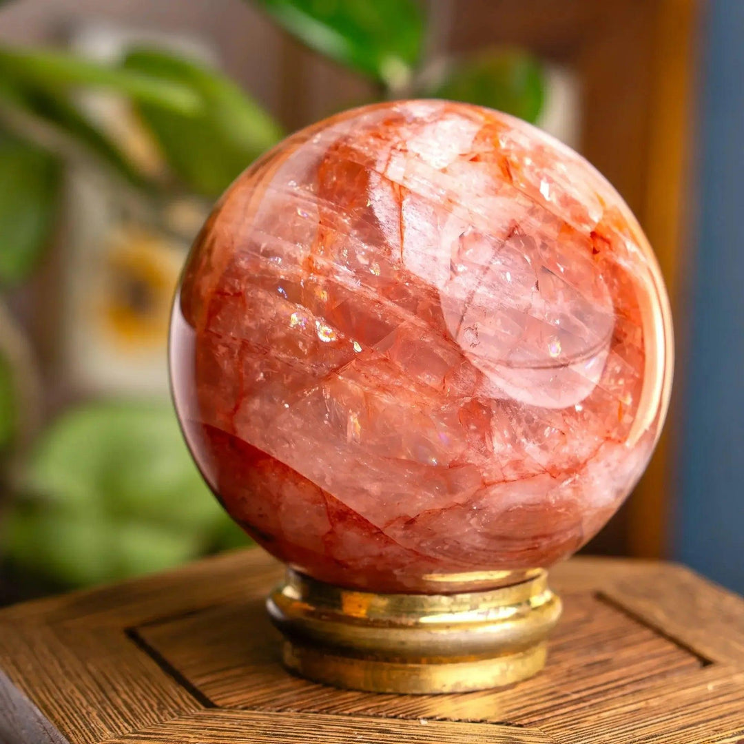 Polished Fire Quartz Hematoid Sphere from Crystal Destiny, with red-orange inclusions on a gold stand.