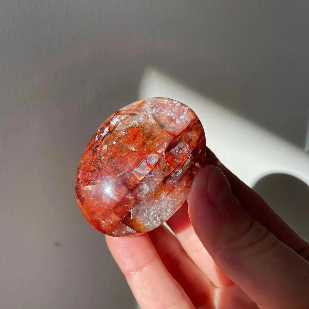 Hand holding a polished Fire Quartz palm stone with fiery red hematite inclusions, radiating warm hues from Crystal Destiny.