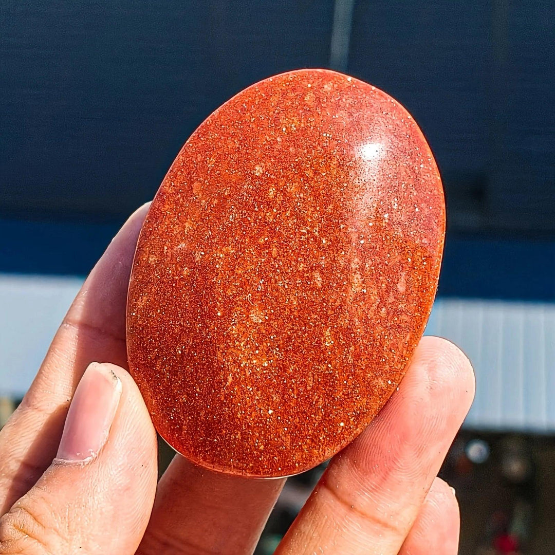 Shimmering orange Fire Sandstone Palm Stone, a polished oval crystal for meditation and healing.