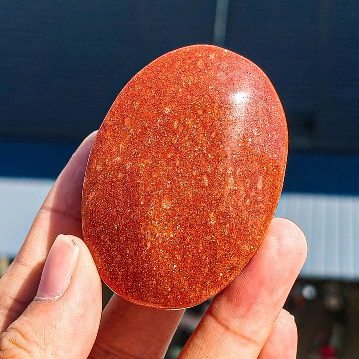 Shimmering orange Fire Sandstone Palm Stone, a polished oval crystal for meditation and healing.