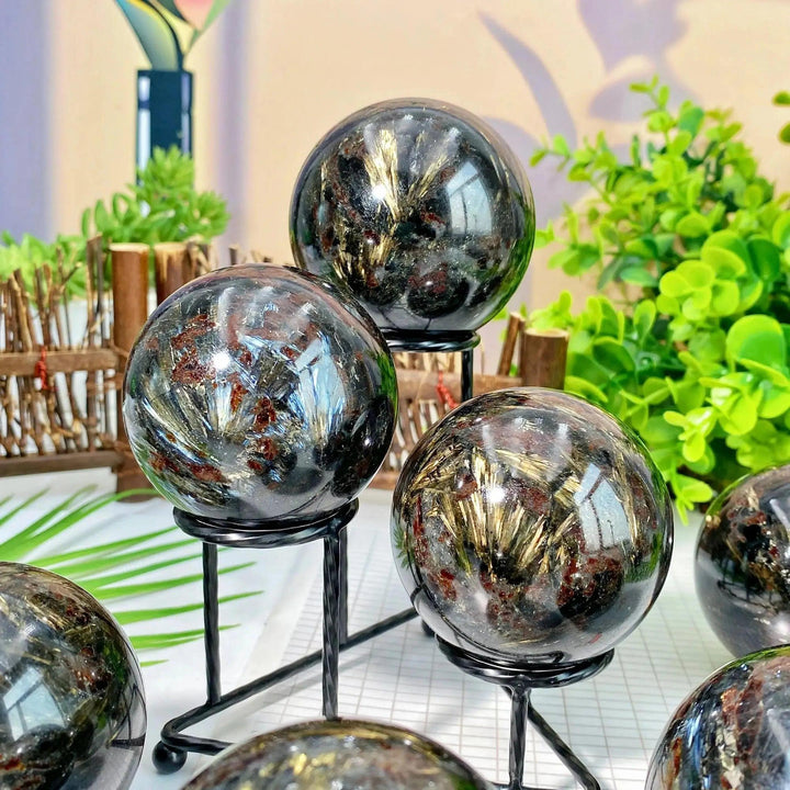 Polished black Firework Jasper crystal spheres with golden bursts, displayed on stands by Crystal Destiny.