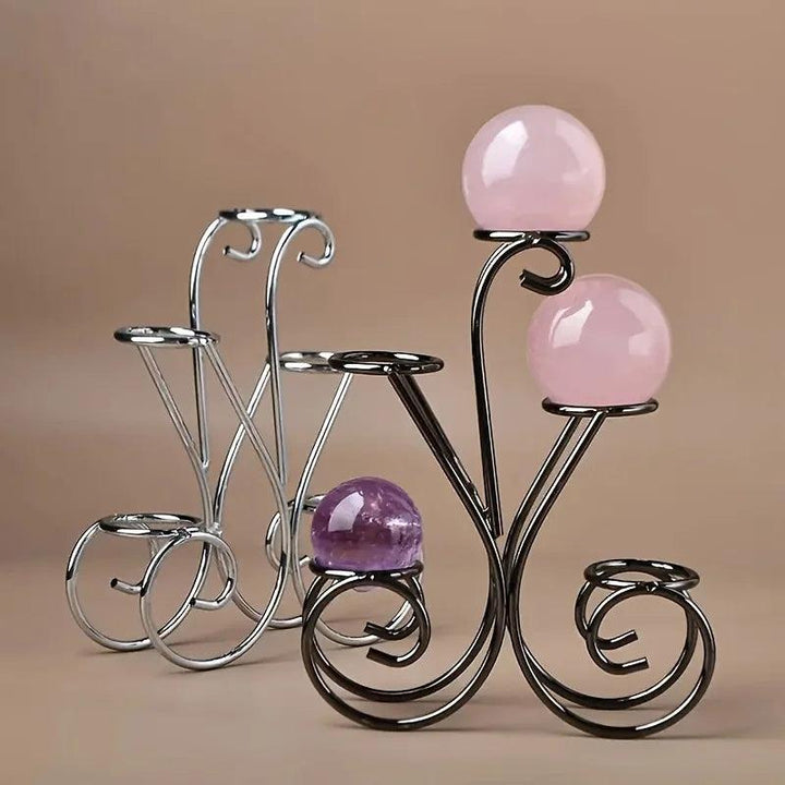 Black and silver metal flower-petal display stands holding pink rose quartz and purple amethyst crystal spheres.