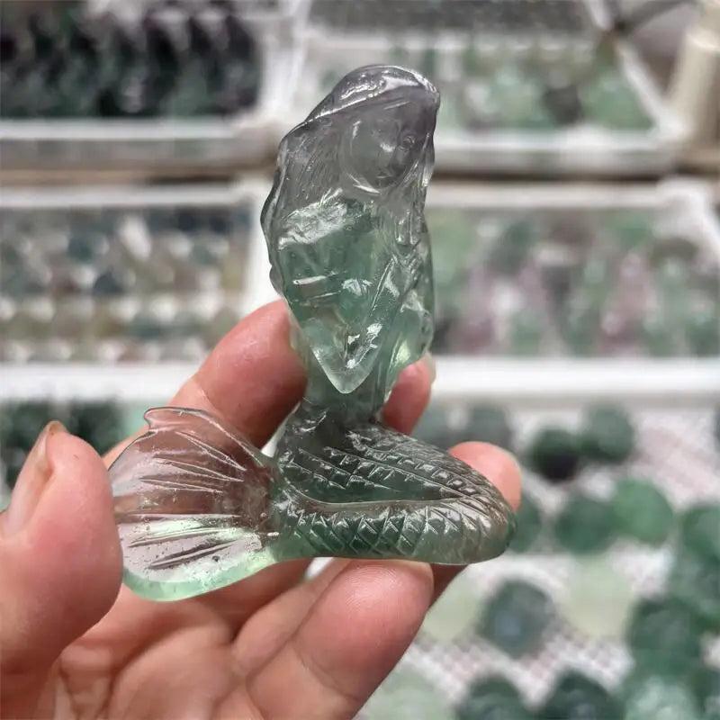 Hand-carved natural fluorite mermaid crystal figurine with translucent green and purple hues for healing and home decor.