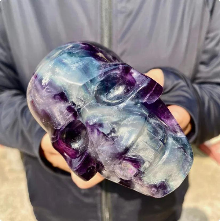 Large Rainbow Fluorite crystal skull carving with flowing bands of purple, blue, green, and cream.