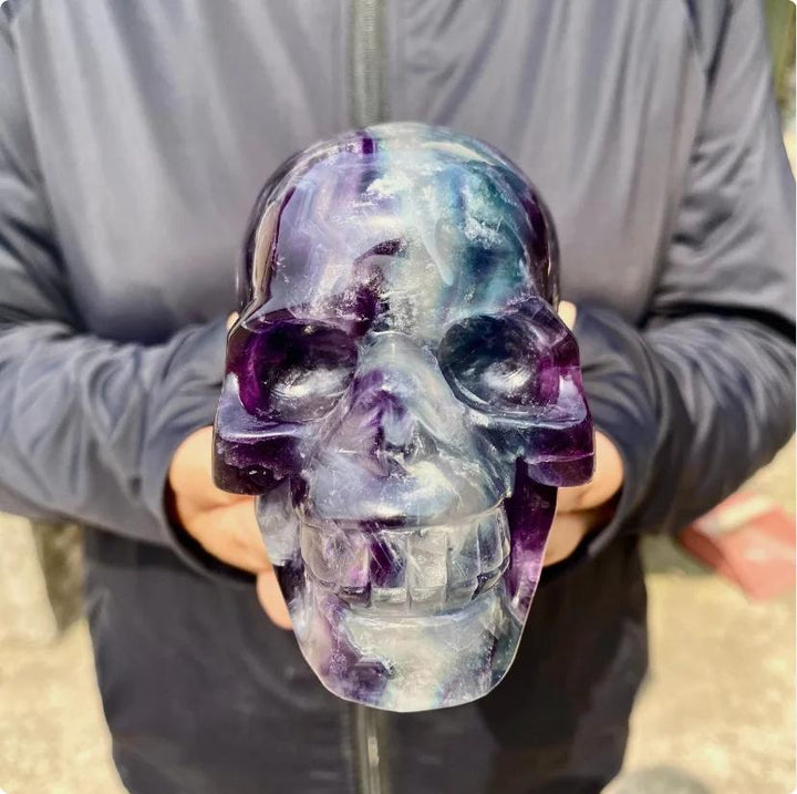 Large Rainbow Fluorite crystal skull carving with flowing purple, blue, green, and cream bands.