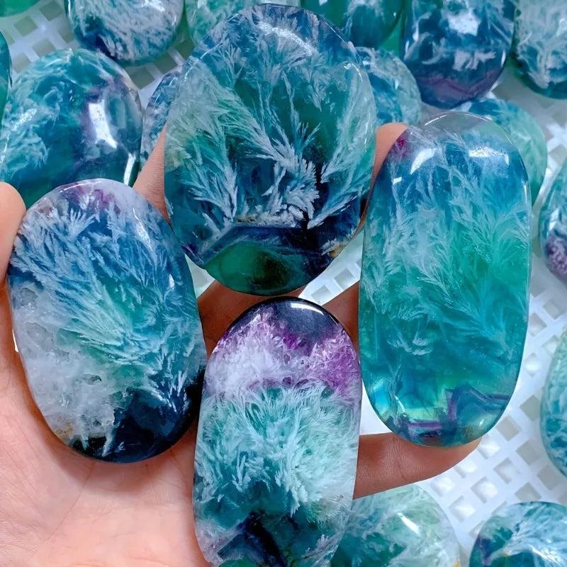 Polished feather snowflake fluorite palm stone with vibrant teal and purple hues, perfect for healing and meditation.