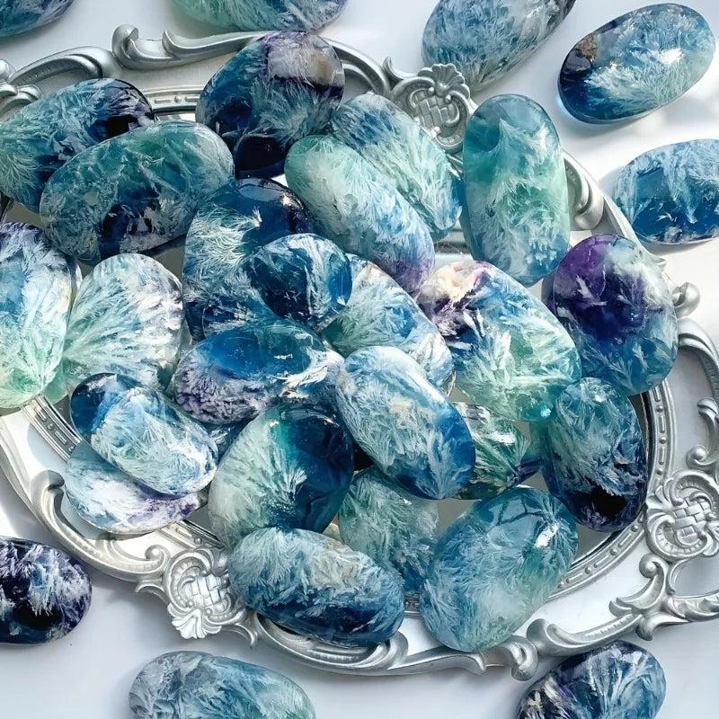Polished feather snowflake fluorite palm stones featuring vibrant blue and purple hues with unique, natural floral patterns.
