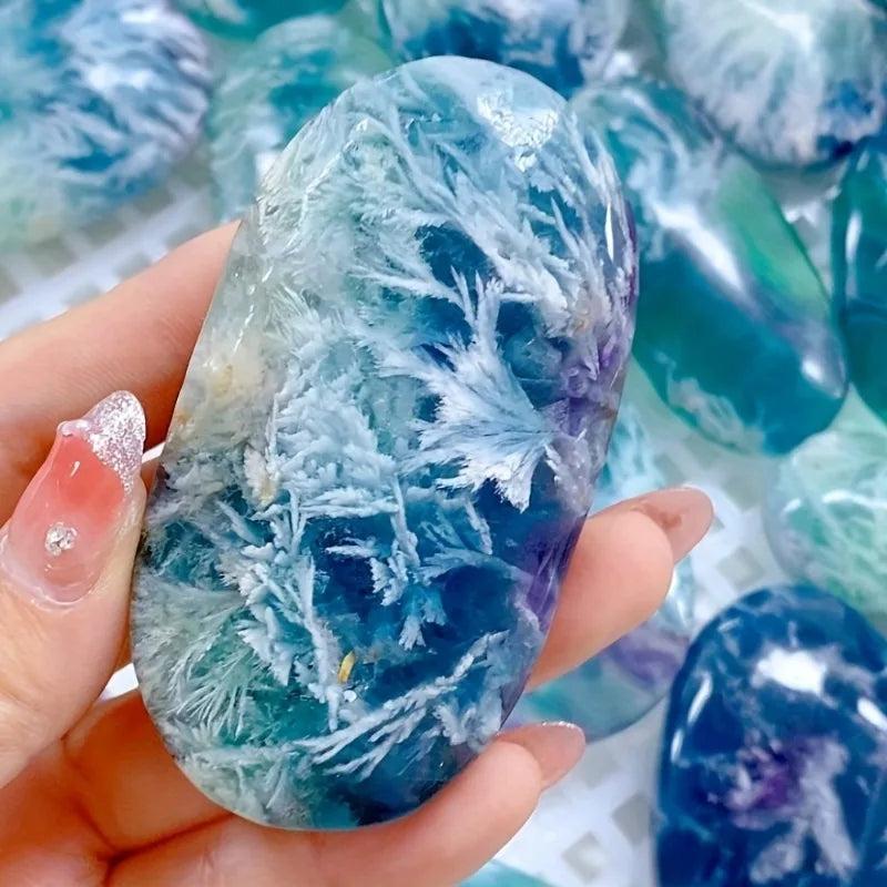 Polished feather snowflake fluorite palm stone featuring vibrant blue and purple hues with unique white crystal patterns.