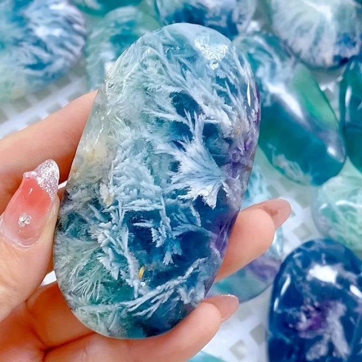 Polished feather snowflake fluorite palm stone featuring vibrant blue and purple hues with unique white crystal patterns.