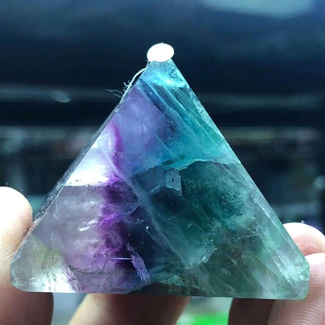 Vibrant Fluorite crystal pyramid, shifting from purple to green to teal, held between fingers.