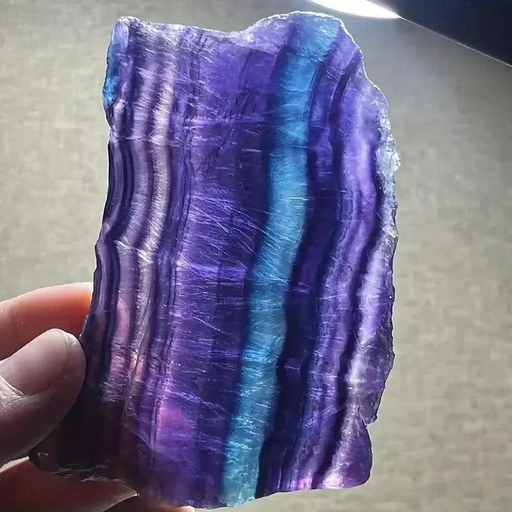 Hand holding a vibrant Fluorite crystal slice with purple, blue, and green bands for mental clarity from Crystal Destiny.