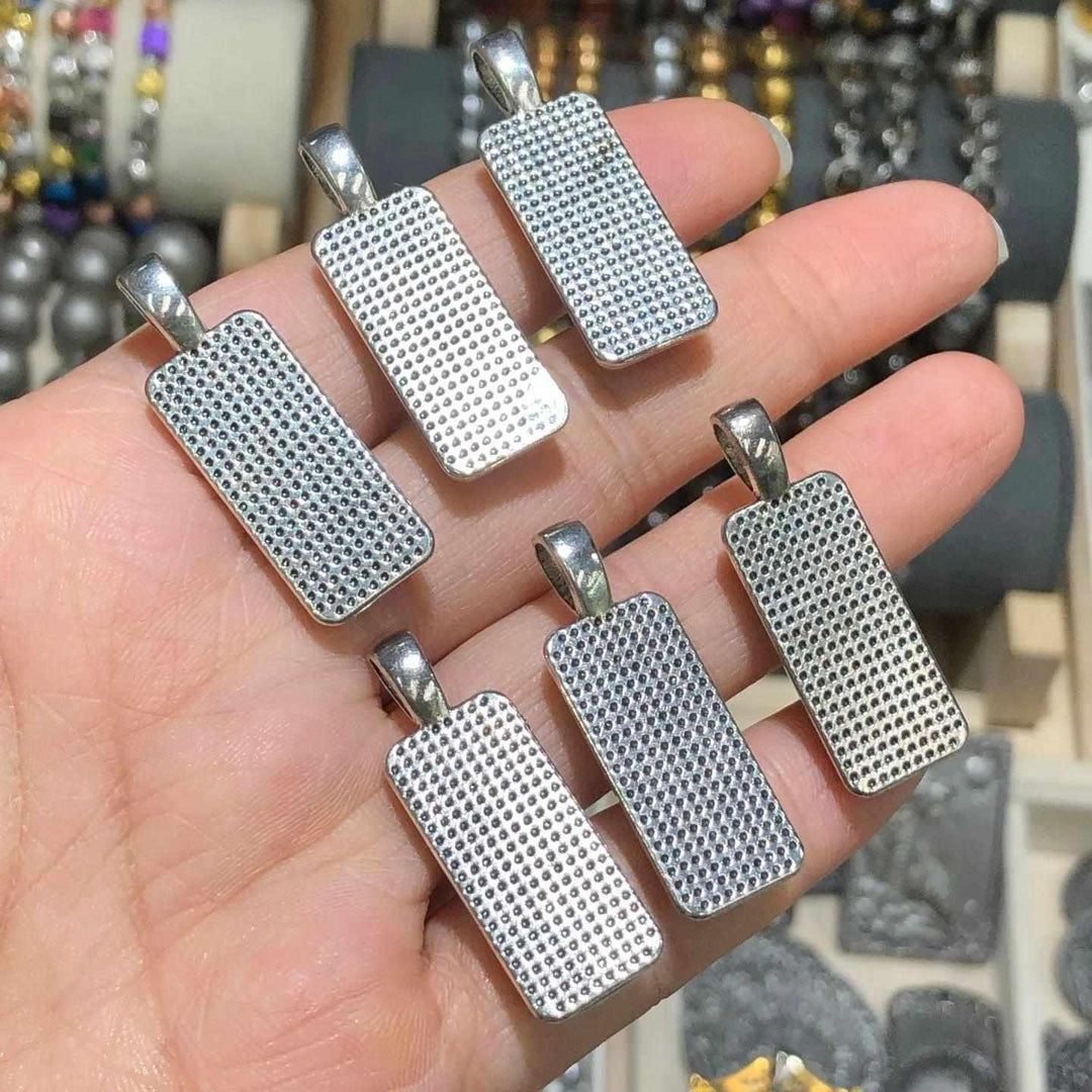 Hand holding Gibeon meteorite rectangle pendants in stainless steel frames featuring unique Widmanstatten patterns.