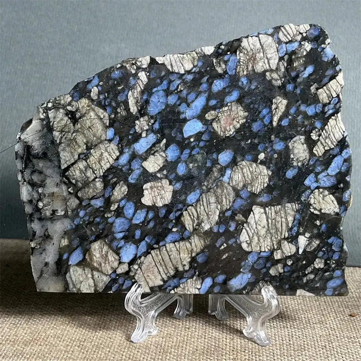 Polished Glaucophane slab from Crystal Destiny, featuring deep blue-gray and white speckled natural crystal on a stand.