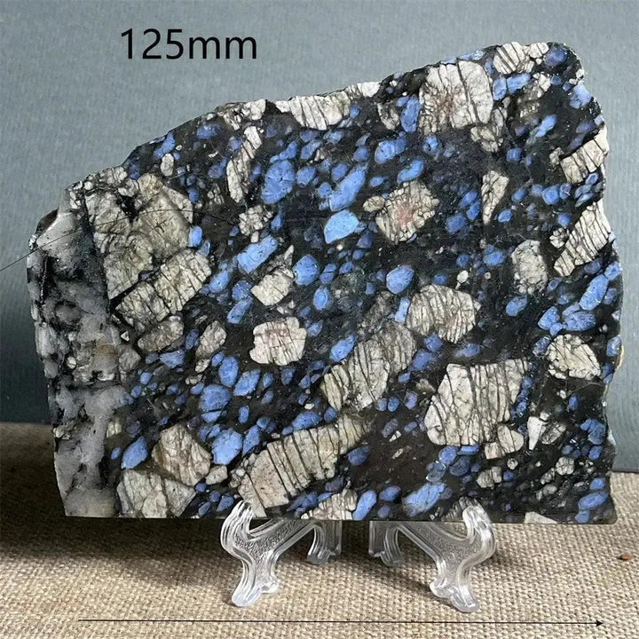 Polished Glaucophane slab from Crystal Destiny, featuring deep blue-gray and white patterns on a clear stand.