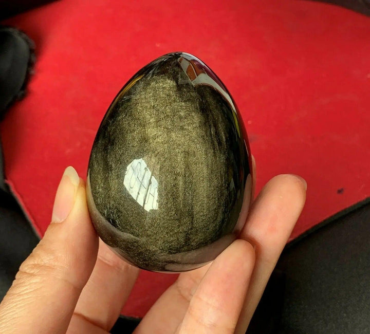 Polished Gold Obsidian Crystal Egg, a volcanic glass with a golden shimmer, held for manifestation and grounding.