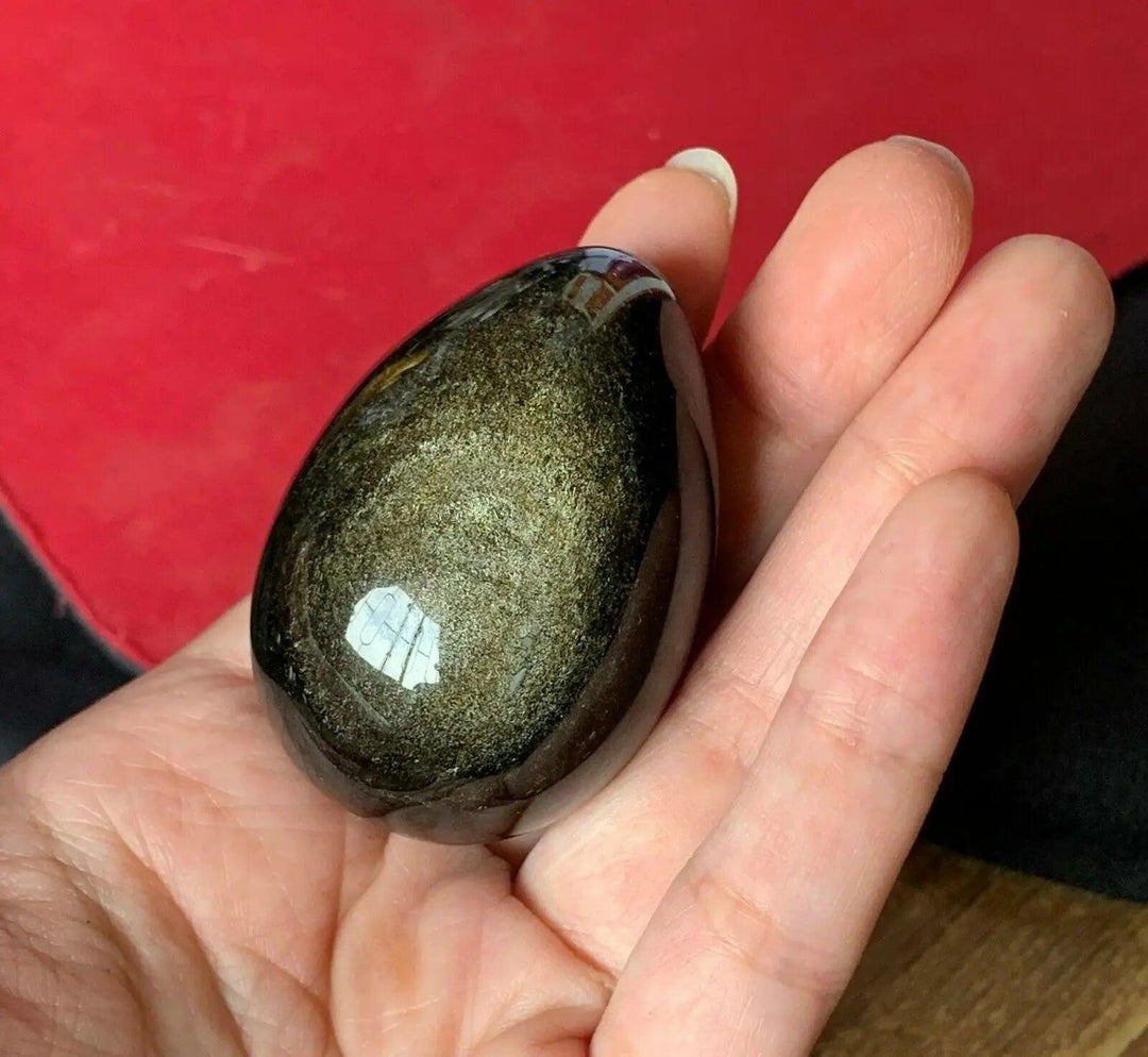 Polished Gold Obsidian Crystal Egg for Manifestation, held in a hand, showcasing its warm, golden shimmer and grounding power.