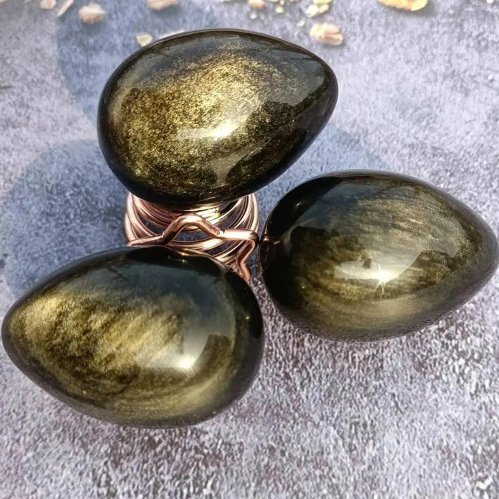 Three polished Gold Obsidian Crystal Eggs, shimmering with golden light, for powerful manifestation and grounding.