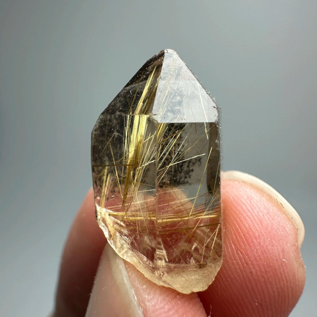 Natural Brazil Gold Rutilated Quartz crystal with golden hair-like inclusions, held between fingers.