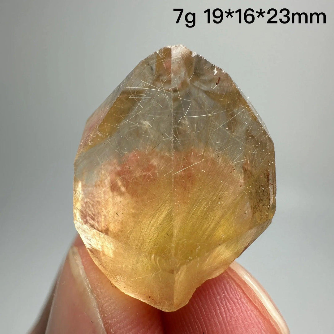 Natural Brazil Gold Rutilated Quartz crystal with hair-like inclusions, held between fingers.