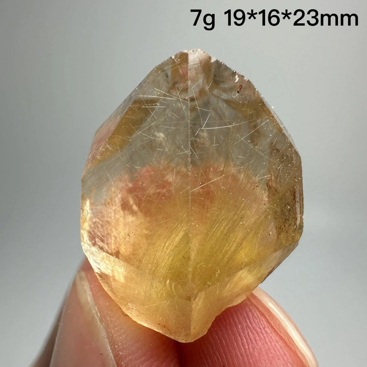 Natural Brazil Gold Rutilated Quartz crystal with hair-like inclusions, held between fingers.