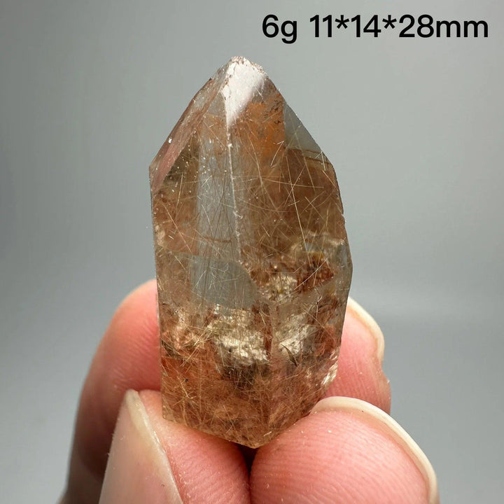 Natural Brazil Gold Rutilated Quartz crystal point with golden rutile inclusions, held between fingers.