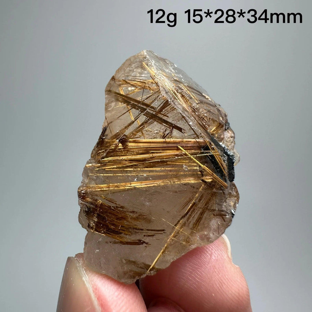 Natural Brazil Gold Rutilated Quartz crystal with golden rutile needles and dark hematite inclusions, held by fingers.