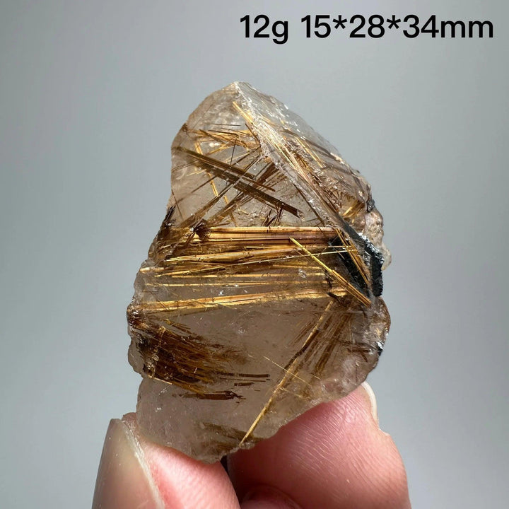 Natural Brazil Gold Rutilated Quartz crystal with golden rutile needles and dark hematite inclusions, held by fingers.