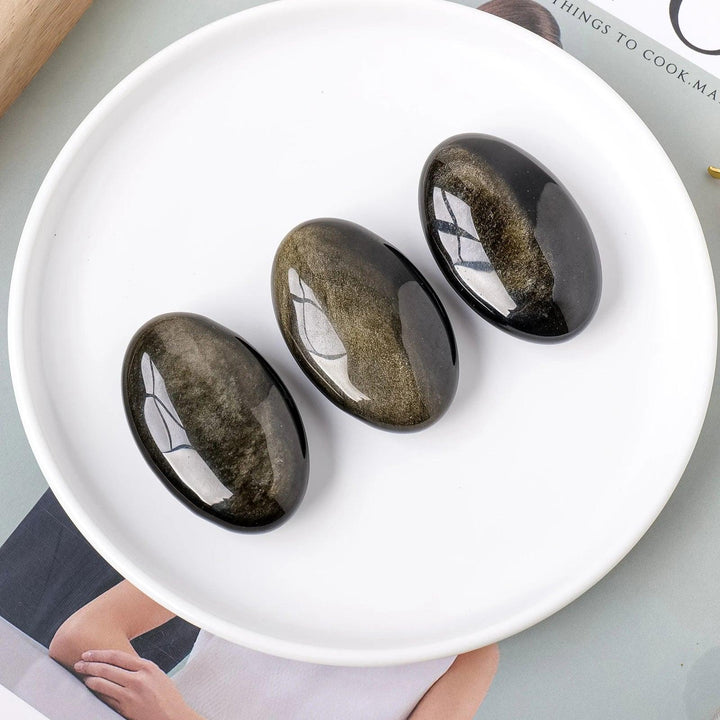Three polished Gold Sheen Obsidian palm stones with a deep black volcanic base and a shimmering golden glow for grounding.